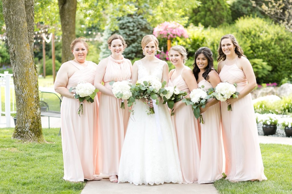 bridesmaids in blush gowns with bride smiling at the camera at wedding atThe Florian Gardens in Eau Claire
