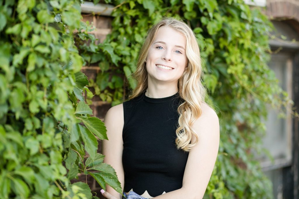 girl leaning against a vine covered brick wall for her senior photos in Eau Claire