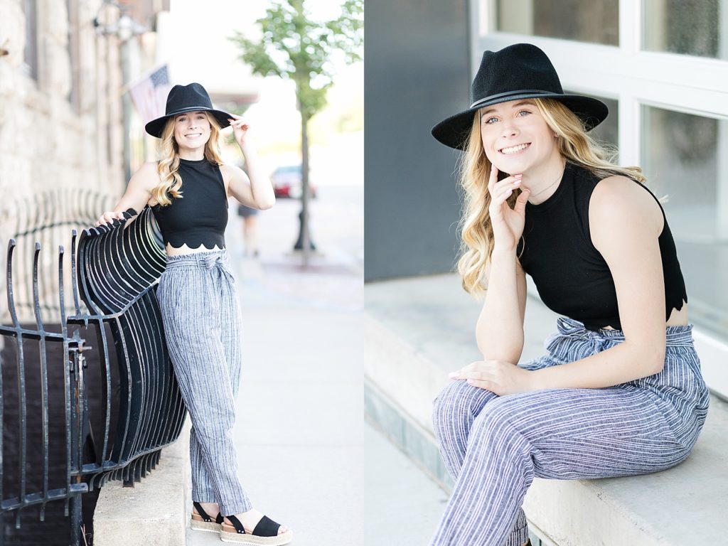 girl leaning against a black railing in Eau Claire with a black hat and outfit on for her senior photos