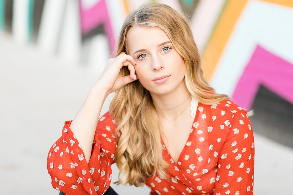 girl with orange floral shirt sitting infront of a bright wall for boho eau claire senior photos