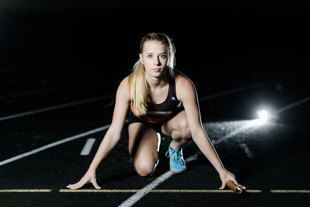 Girl in starting position for relay with baton in night senior photo