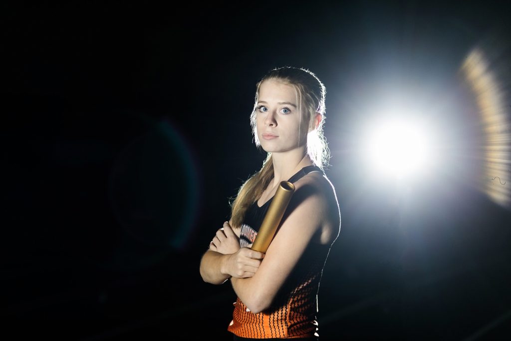 girl holding baton in night shot for relay team Bloomer Blackhawks jersey on