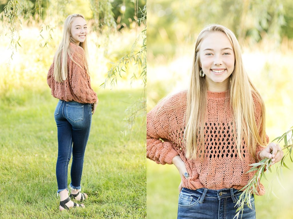 girl looking over her shoulder and at camera in an orange sweater and jeans for her Eau Claire boho senior photos
