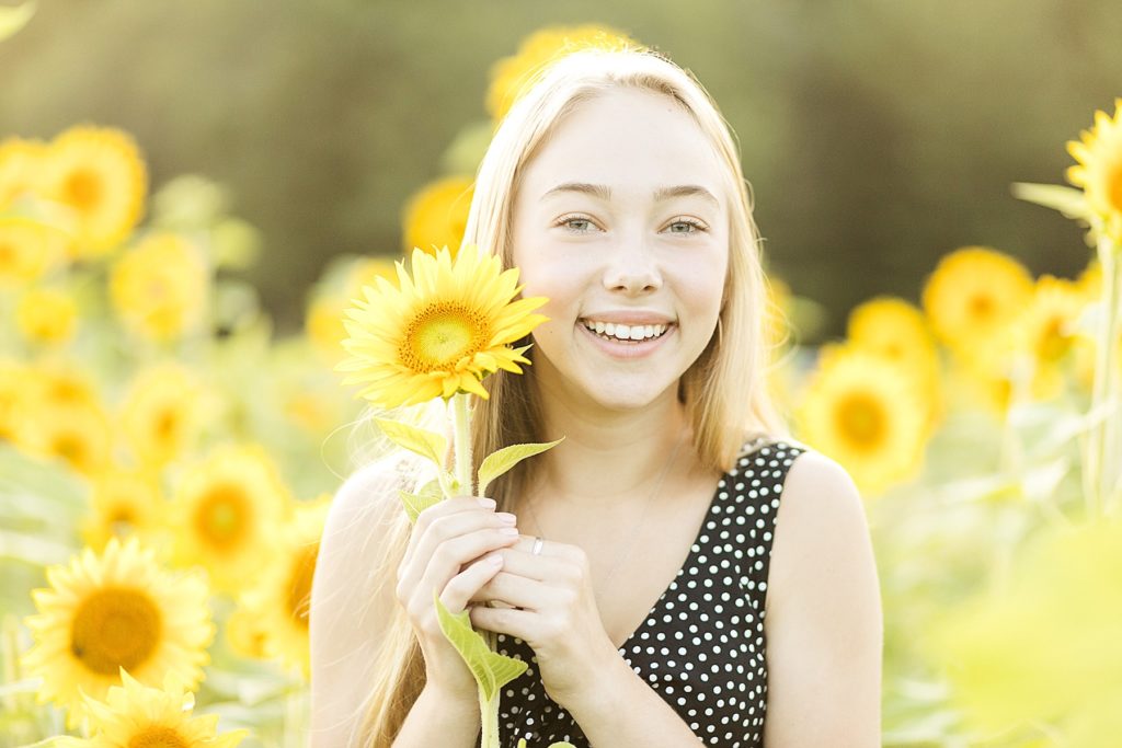 girl peeking around a sunflower for her Eau Claire boho senior photos