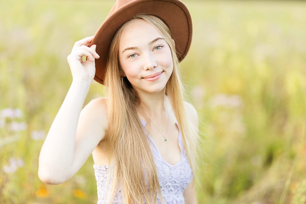 girl with brown hat and purple Free People dress in a field of flowers looking at the camera for her Eau Claire boho senior photos