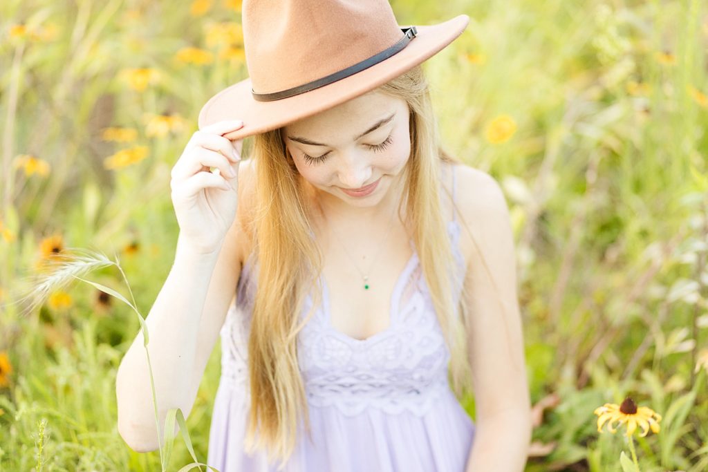 girl in a brown hat looking down in a field of flowers with a purple Free People dress for her Eau Claire boho senior photos