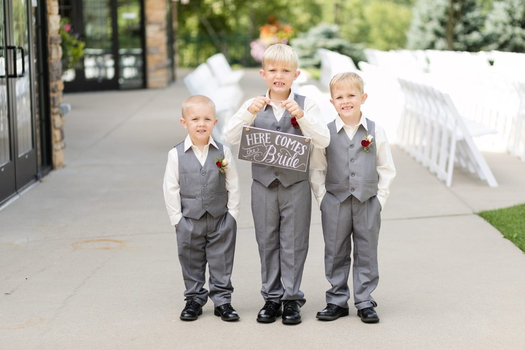 ring bearers getting ready to walk down the aisle holding a sign that says "here comes the bride"
