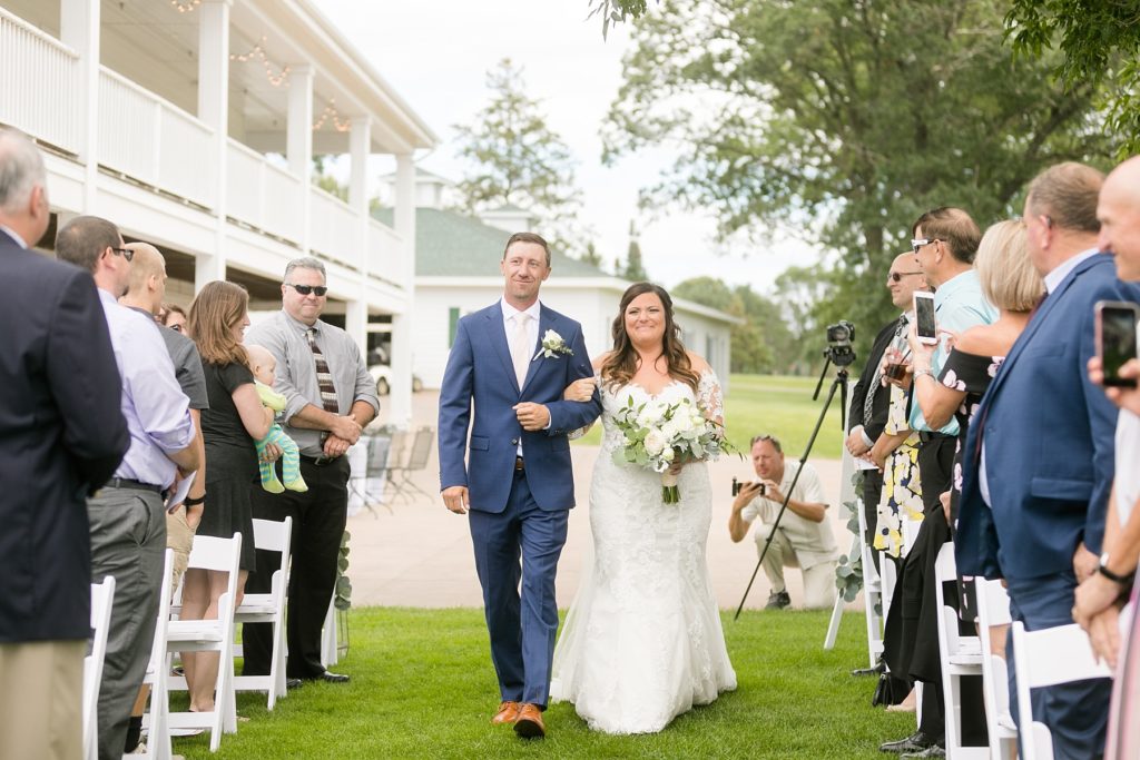 bride walking down the aisle with her brother outside by the lake at Lake Wissota Golf & Events