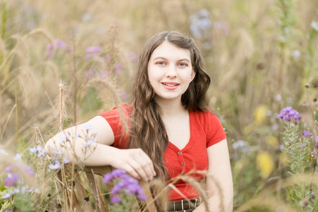 girl in orange shirt sitting in a field of fall flowers for her Cadott High School senior photos