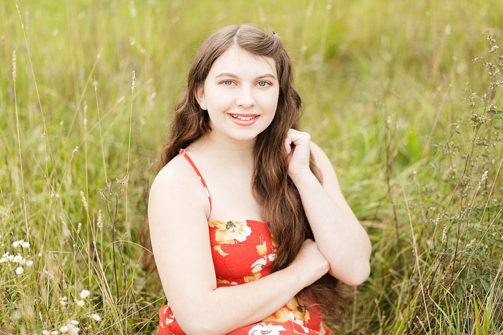 girl sitting in a field in a red dress with yellow flowers for her Cadott High School senior photos