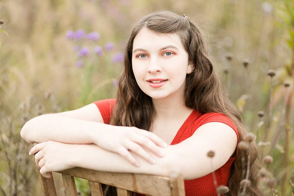 girl sitting backwards on an antique wooden chair in a field of flowers for her Cadott High School senior photos