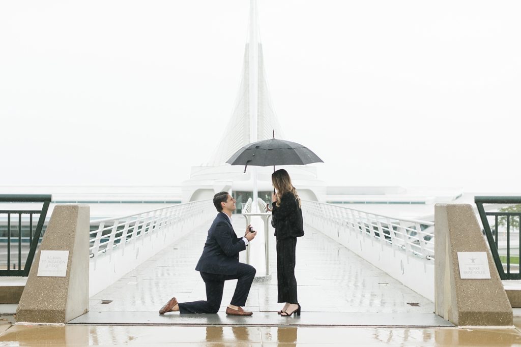 guy on one knee proposing to girl in the rain at the Milwaukee Art Museum