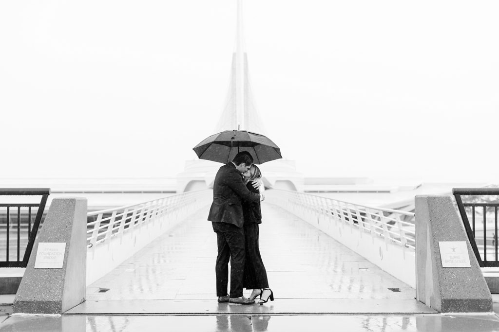 couple kissing in a black and white photo in the rain after he proposes at the Milwaukee Art Museum