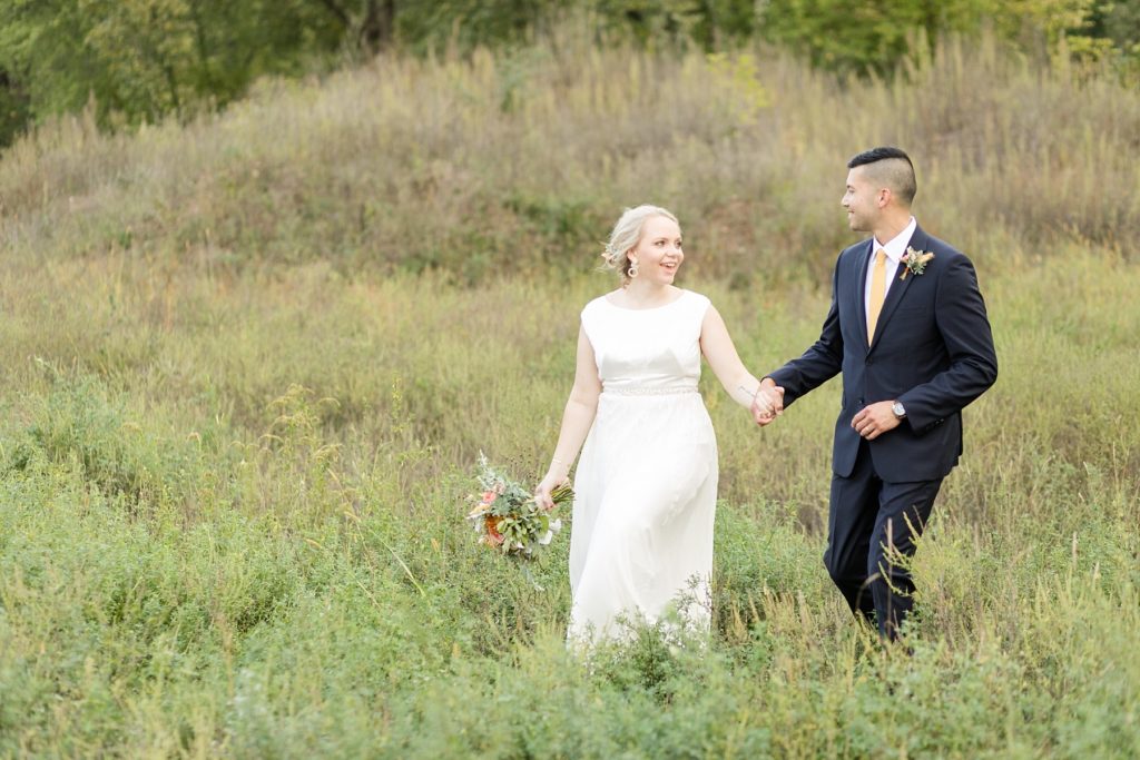 couple in a field smiling at each other and walking at their wedding at the Oxbow Hotel in Eau Claire