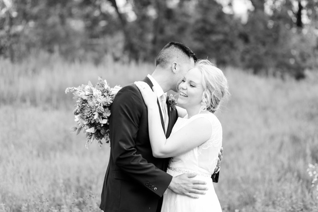 bride laughing at what the groom is whispering in her ear in a black and white photo at their wedding at the Oxbow Hotel in Eau Claire