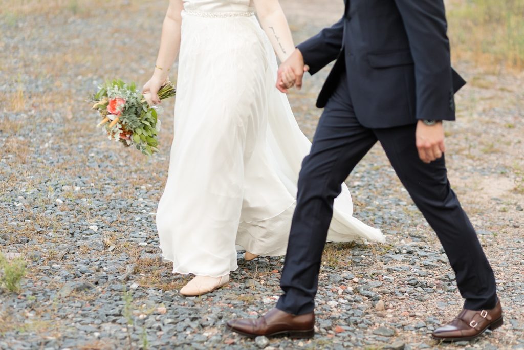 couple walking with wedding bouquet through gravel at their wedding at the Oxbow Hotel in Eau Claire