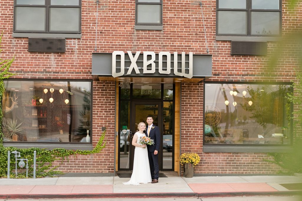 couple smiling at the camera standing infront of the Oxbow Hotel at their wedding at the Oxbow Hotel in Eau Claire