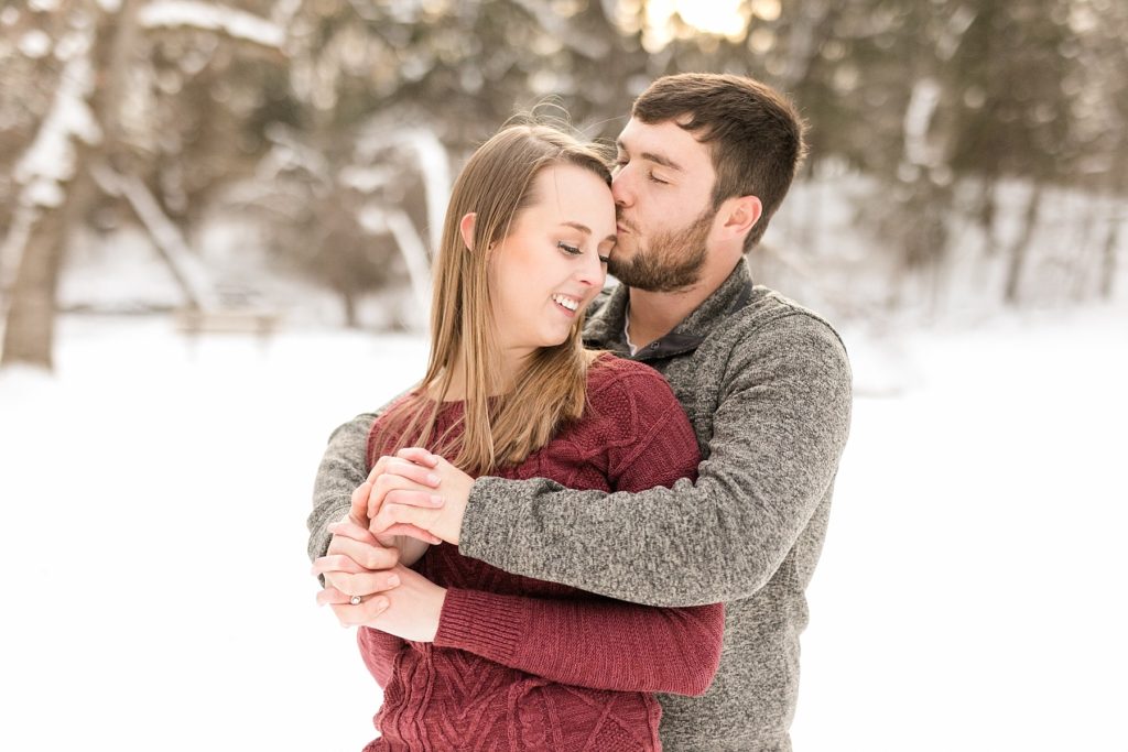 guy kissing girls forehead outside in the snow for their winter Wisconsin engagement photos