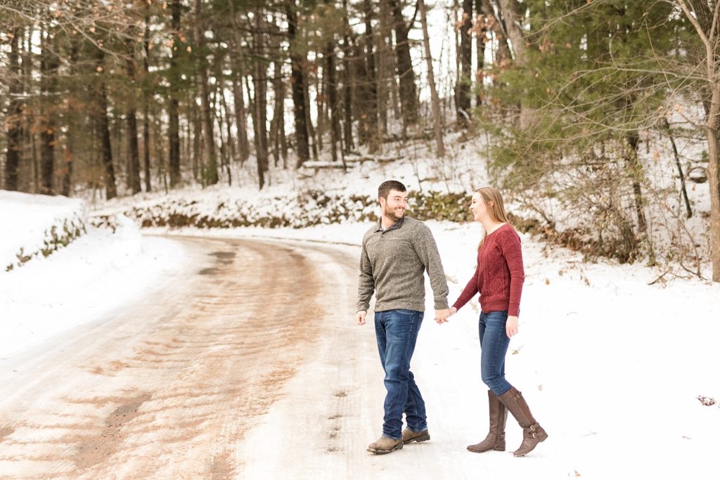 couple crossing a snow covered road for their winter engagement photos in Wisconsin