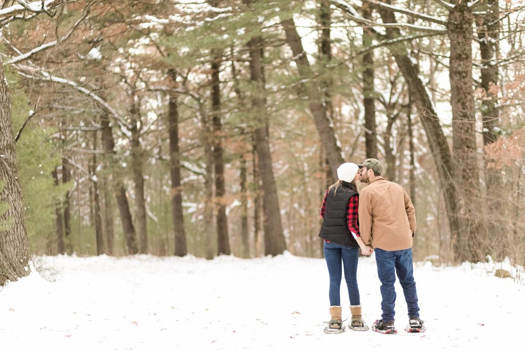 couple kissing in the woods with their snowshoes on for their Wisconsin winter engagement session