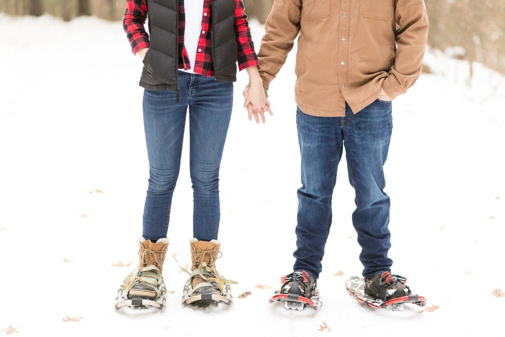 couple holding hands with snowshoes on their feet for their snowshoe engagement session in Wisconsin