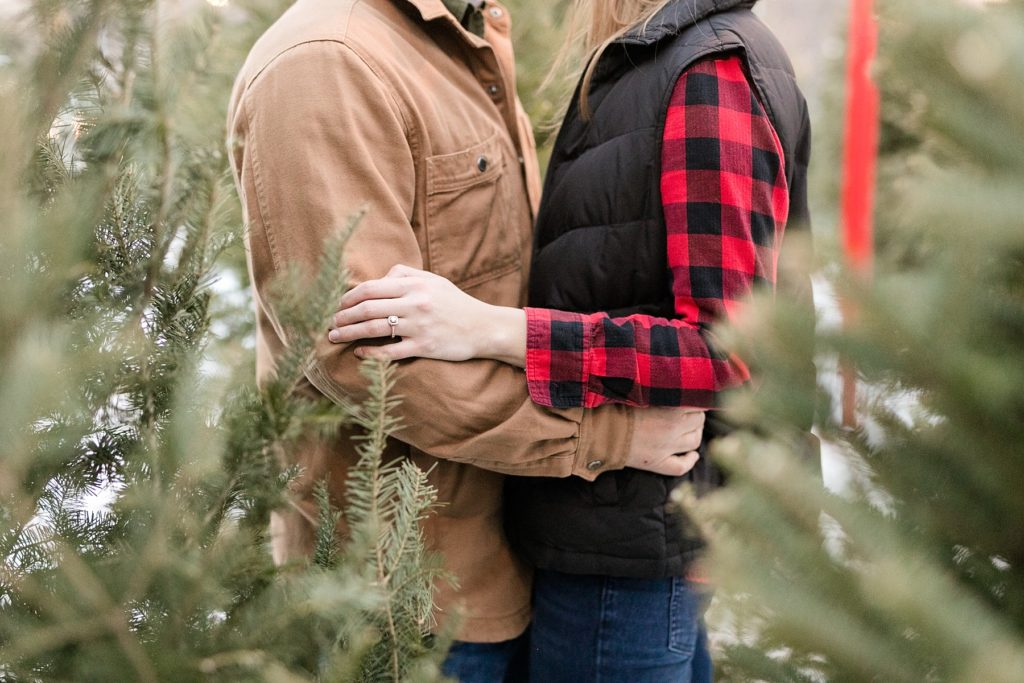 couple cuddling in the Christmas trees for sale in Eau Claire WI