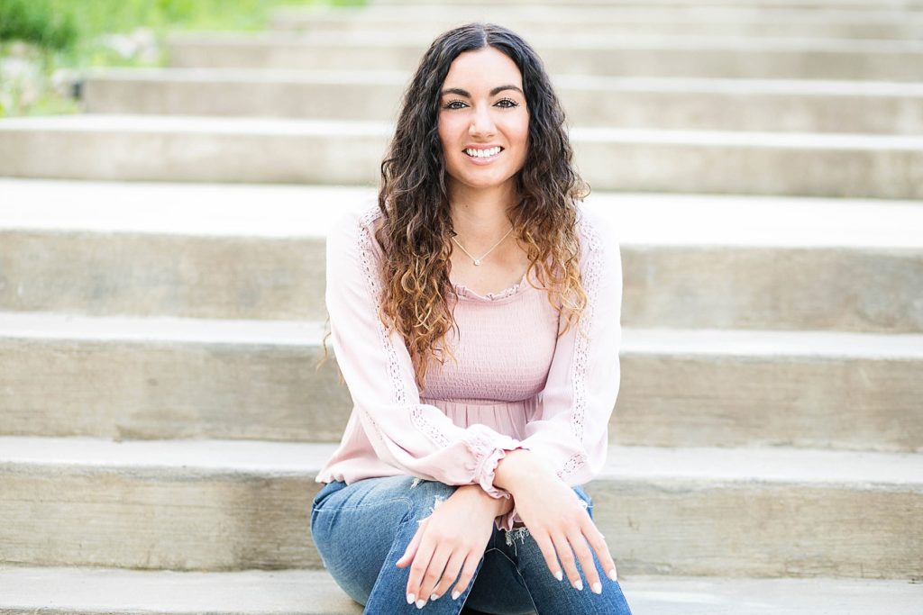 girl in a pink top and jeans sitting on some concrete stairs for her Eau Claire senior photos