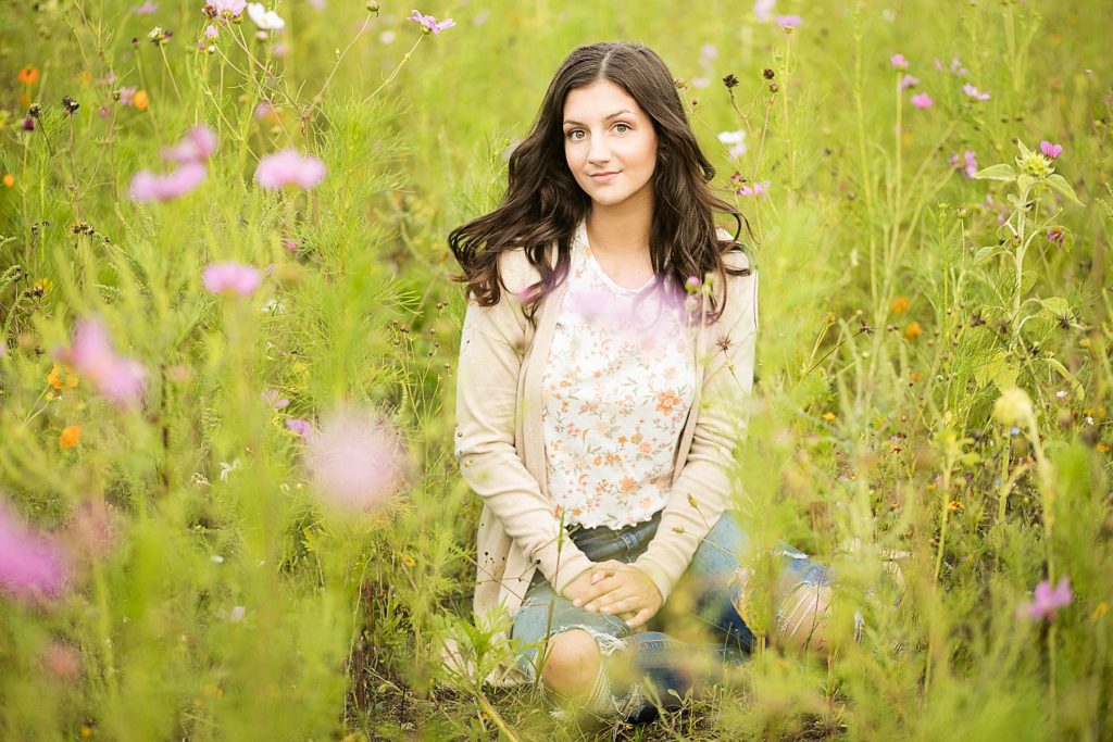 girl sitting in a field of purple and yellow flowers with a cardigan on and the wind blowing in her hair in Chetek WI