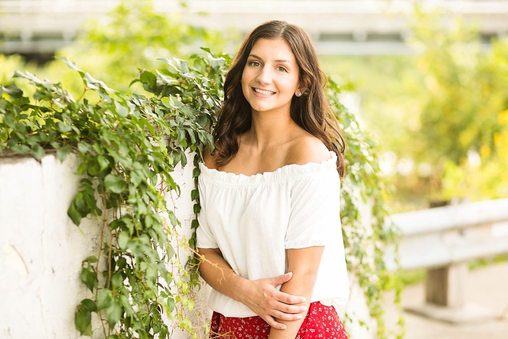 girl standing against a white wall with vines for her Bloomer summer senior pictures