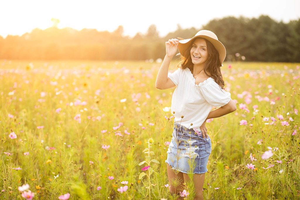 girl laughing in a field of flowers with a hat on and a white shirt and mini denim skirt in Chetek WI
