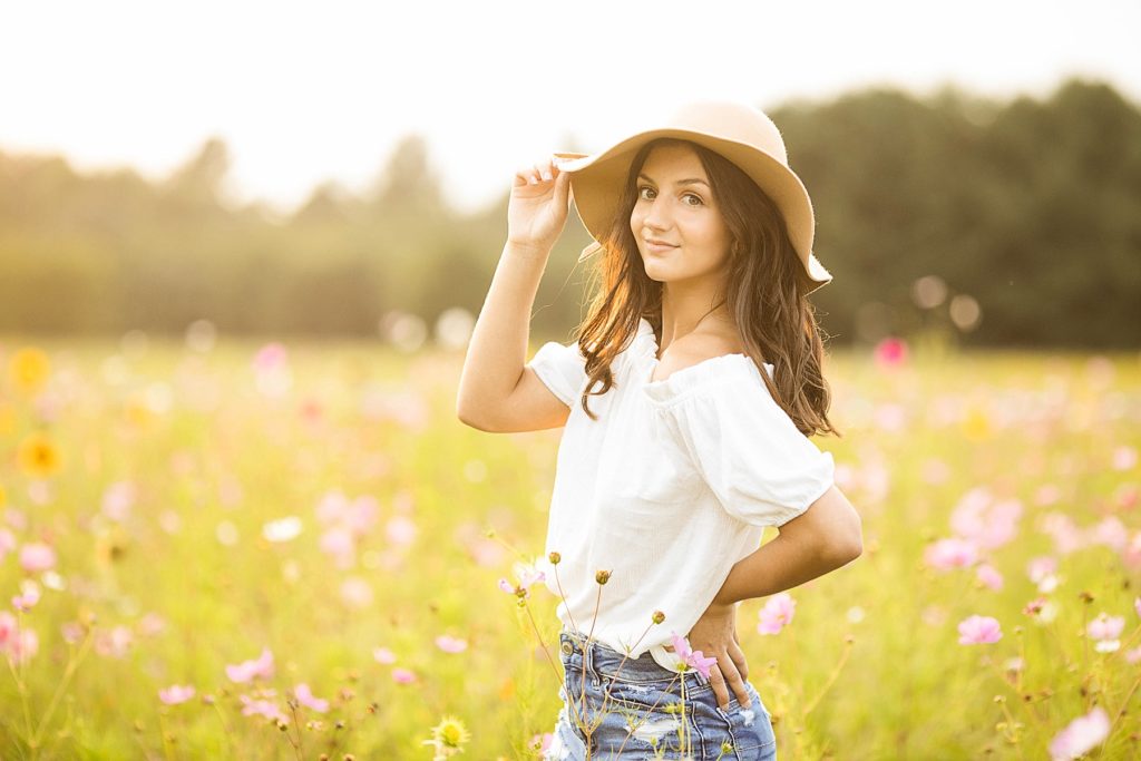 girl with a brown hat on smiling at the camera in a field of flowers in Chetek WI for her senior photos