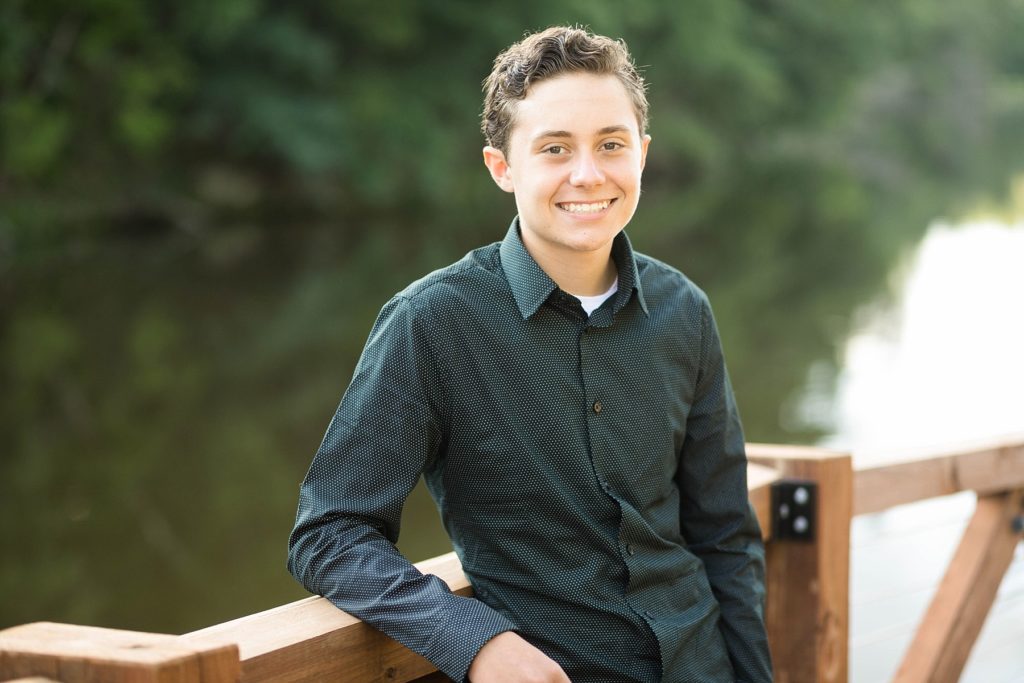boy leaning against the rail of a dock at Irvine Park for his senior photos in Chippewa Falls, WI