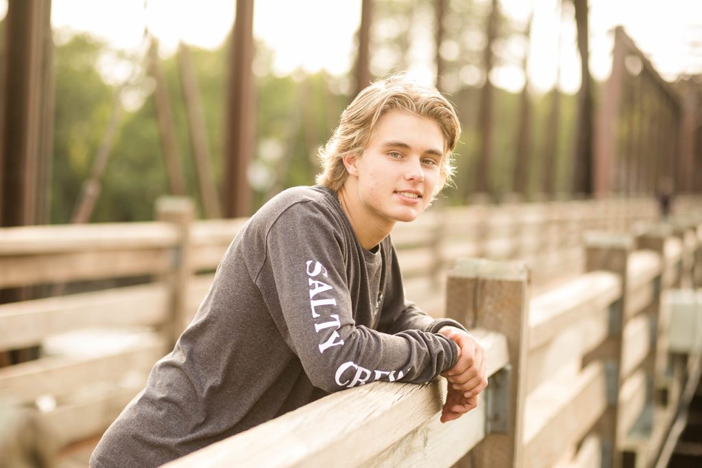 boy leaning on the trestle bridge in Phoenix Park for his senior photos in Eau Claire