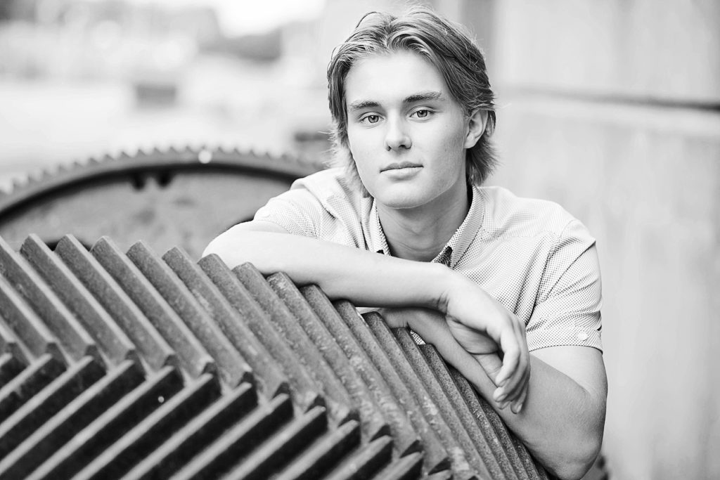 boy leaning on a gear in a black and white photo for his senior photos in Eau Claire, WI