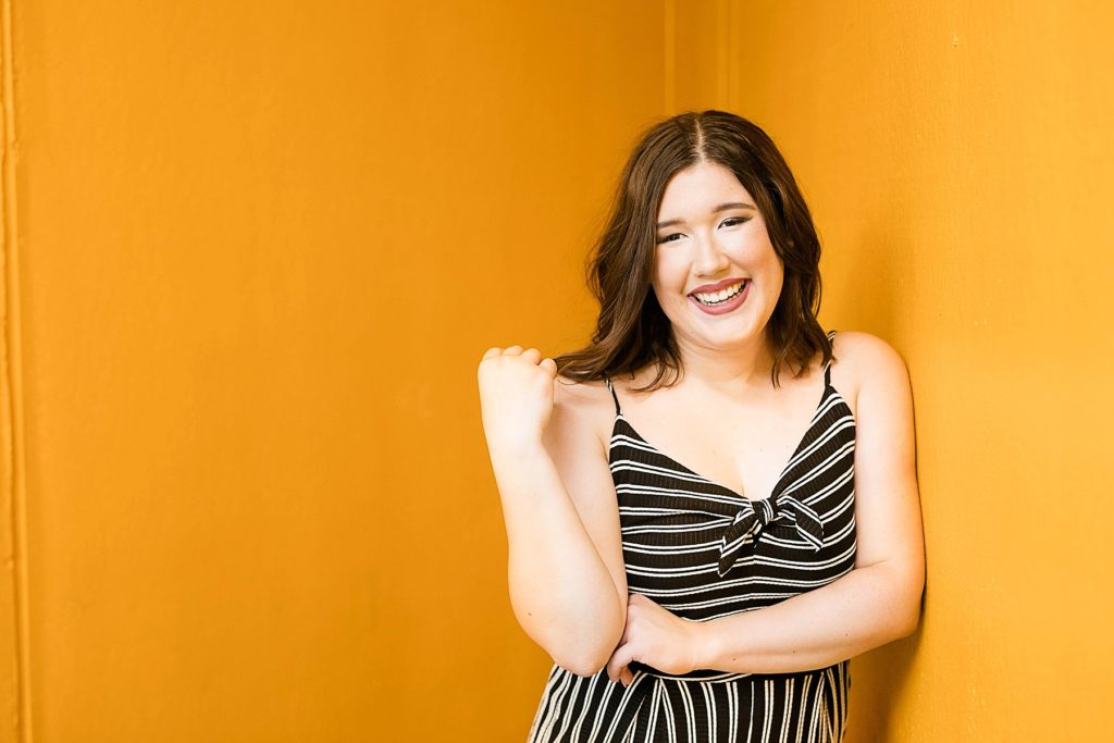 girl leaning on a yellow wall laughing in a black and white outfit in Eau Claire for her laid back senior photos