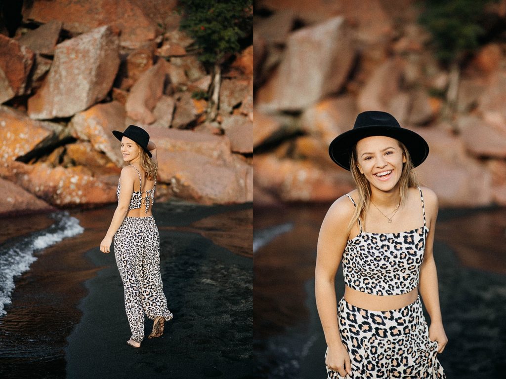 girl stands on a black sand beach on Lake Superior with a black hat on for her North Shore senior pictures