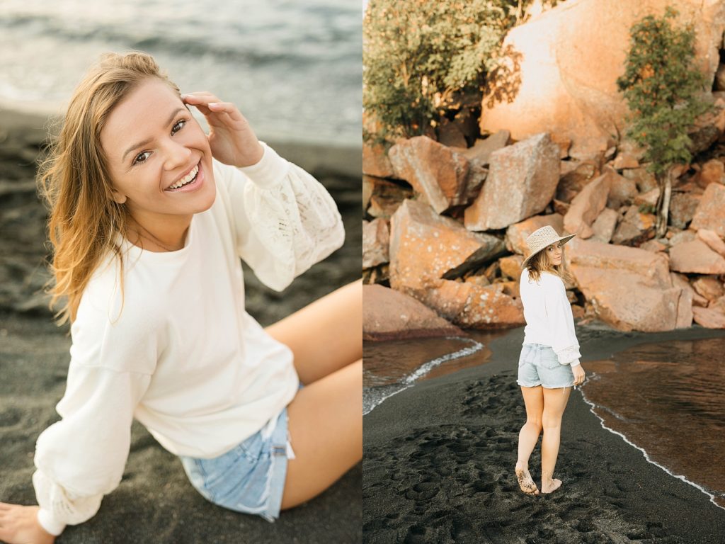 girl sits in on a black sand beach on Lake Superior with shorts on for her North Shore senior pictures