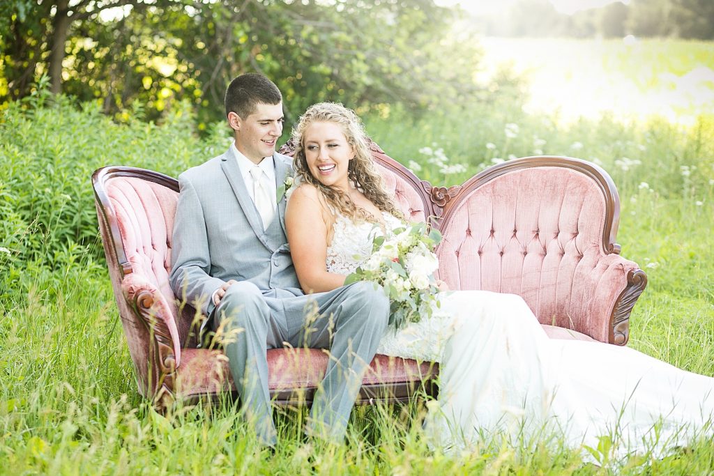 couple sitting on a rented couch from Sweet Legacy in Eau Claire at their summer wedding at The Florian Gardens