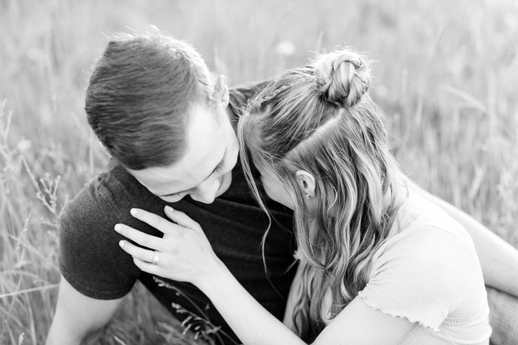 couple sitting in a field laughing in a black and white photo at Willow River State Park in Hudson, WI for their engagement session