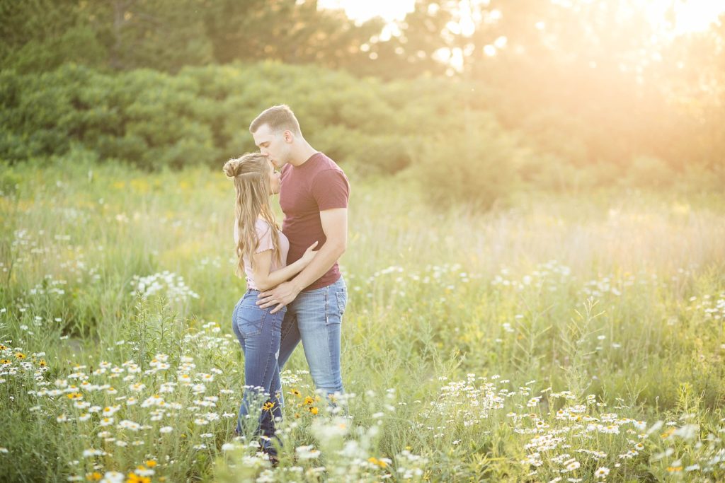 couple kissing in a field of flowers with hazy sun at Willow River State Park in Hudson, WI for their engagement session