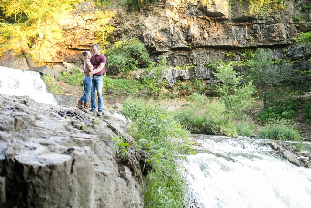 willow river state park in hudson wi couple standing on the edge of the waterfall for their engagement photos