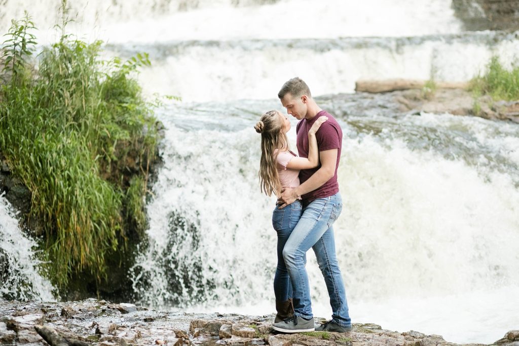willow river state park in hudson wi couple standing on waterfall for their engagement photos