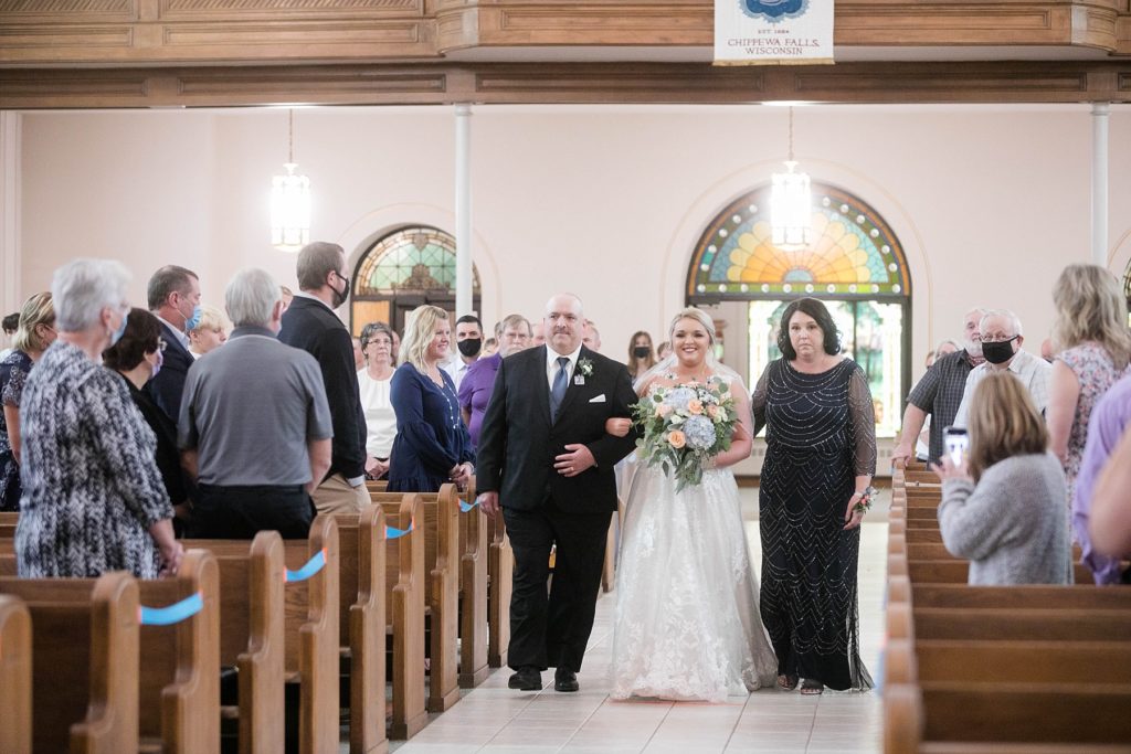 mother and father walk daughter down the aisle at St. Charles of Borromeo in Chippewa Falls for their wedding