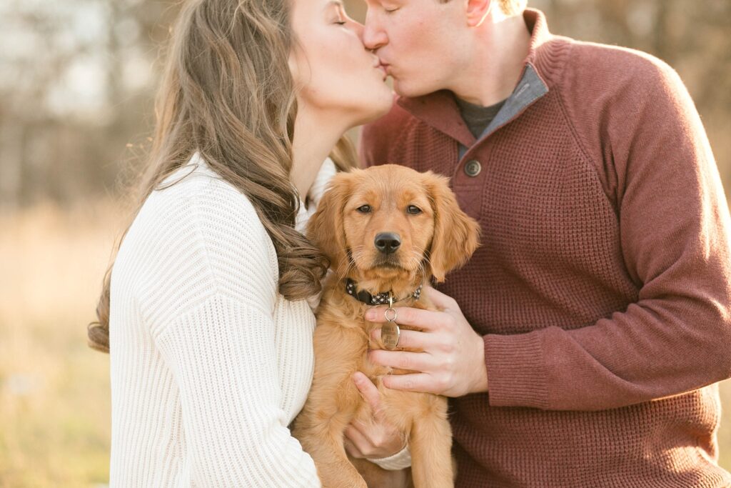 couple kissing with golden retriever between them for their Eau Claire couples session with new puppy