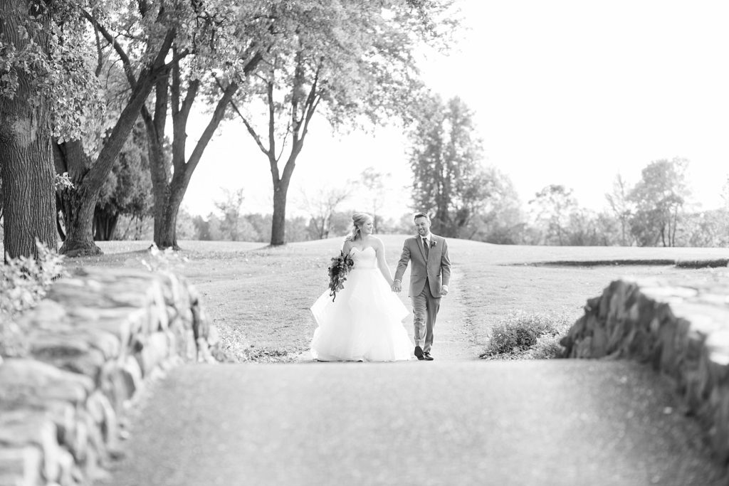black and white photo of the wedding couple walking over the stone bridge at a wedding at Lake Wissota Golf & Events