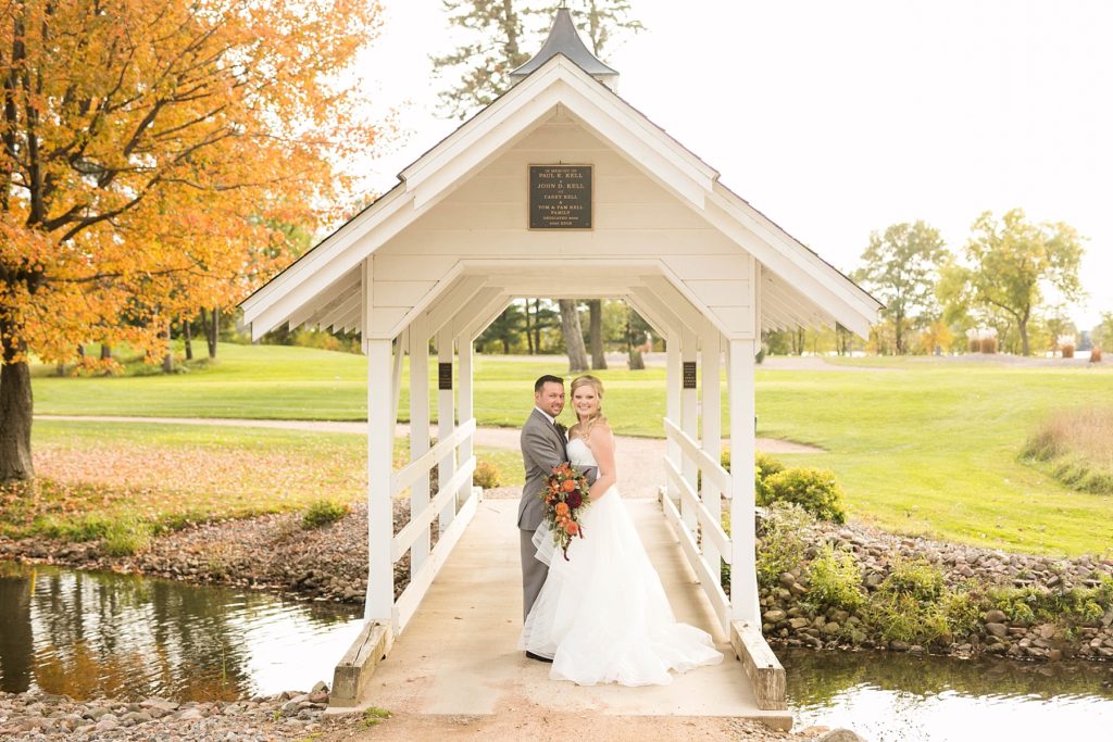 couple standing on the white bridge on the golf course on a fall wedding day at a wedding at Lake Wissota Golf & Events