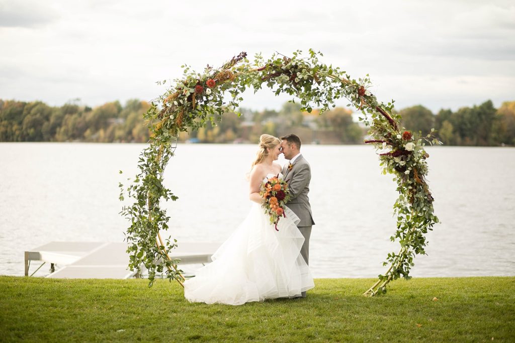 couple under their circle arch with florals hanging off of it by Allure Premiere Event Florists at a wedding at Lake Wissota Golf & Events