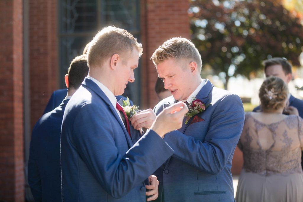 groom and his twin brother pinning their flowers at stunning wedding in Marathon, WI at St. Mary's Catholic Church
