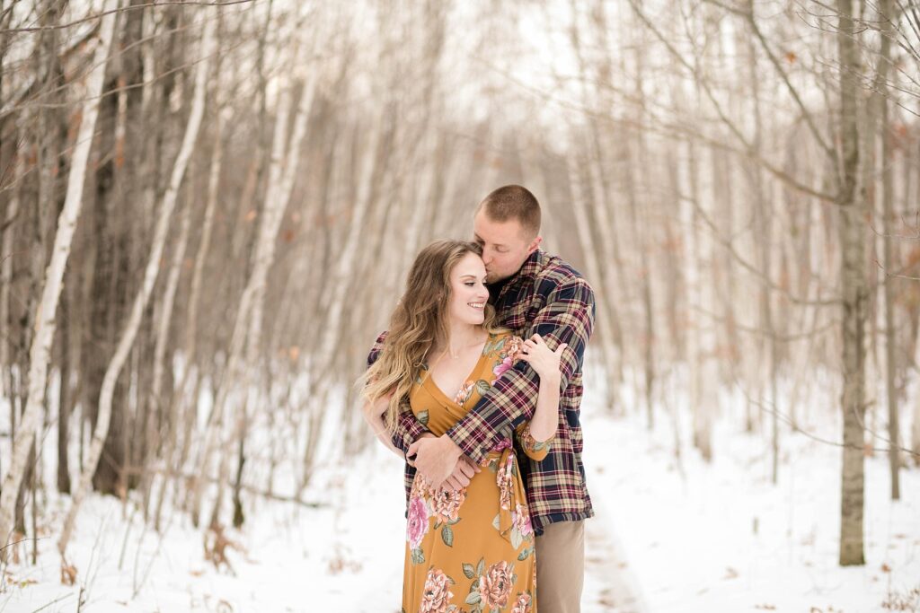 couple kissing in the middle of birch trees on a path for their winter engagement session in Ladysmith