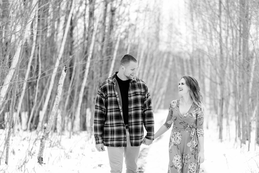 couple walking and laughing in a black and white photo in birch trees for their winter engagement session in Ladysmith